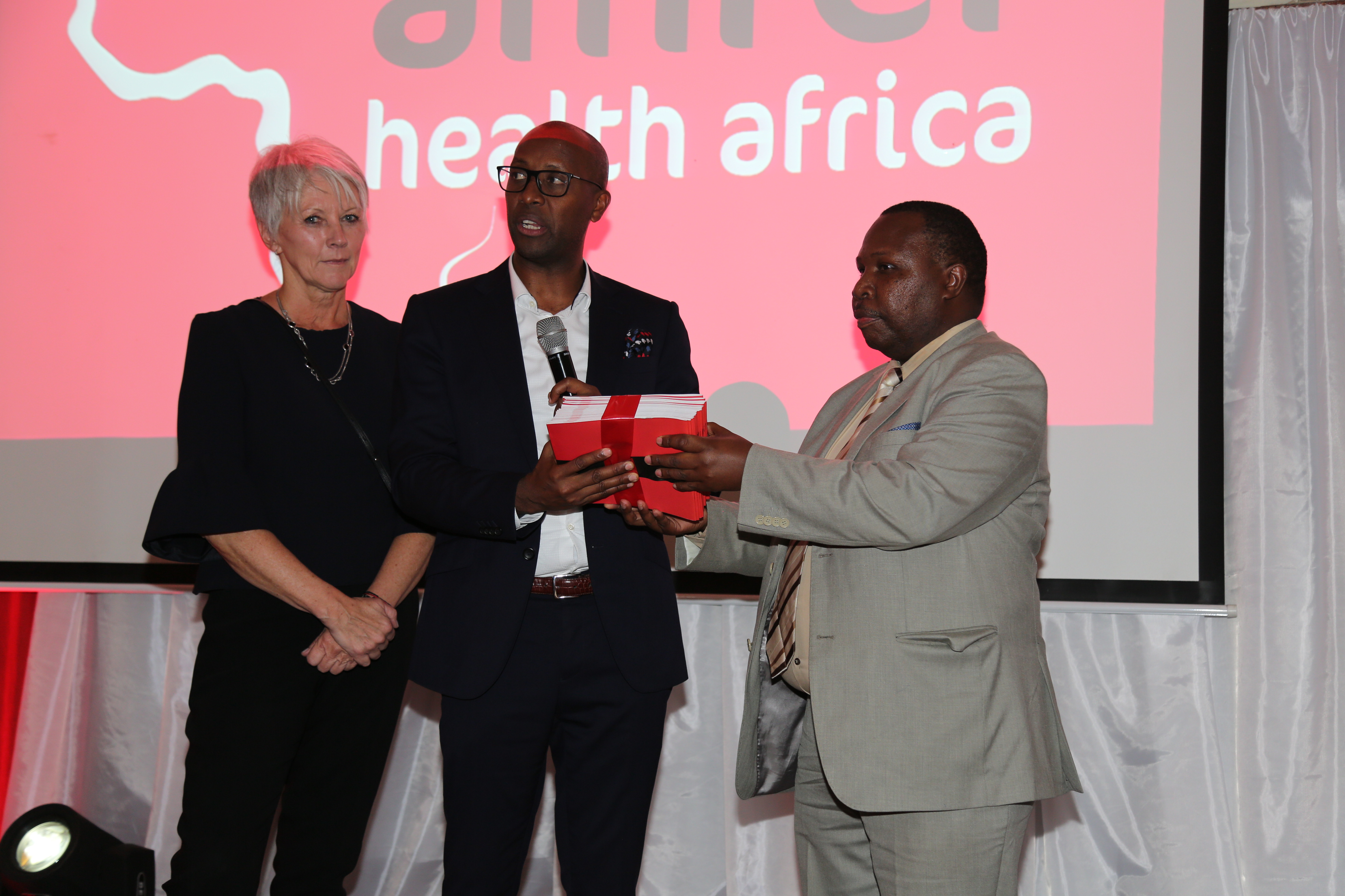 Amref global CEO Dr Gitahi Githinji (middle), hand over the strategy to Head of Directorate of UHC and Health Financing in the Ministry of Health Dr David Kariuki (right) as Amref International Board Vice Chair Mary Anne Mackenzie looks on .